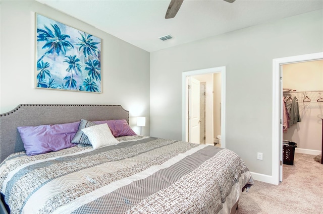 bedroom with a closet, ensuite bath, a spacious closet, light colored carpet, and ceiling fan