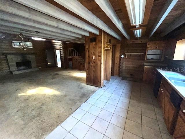 kitchen with beamed ceiling, sink, wood walls, and light tile floors