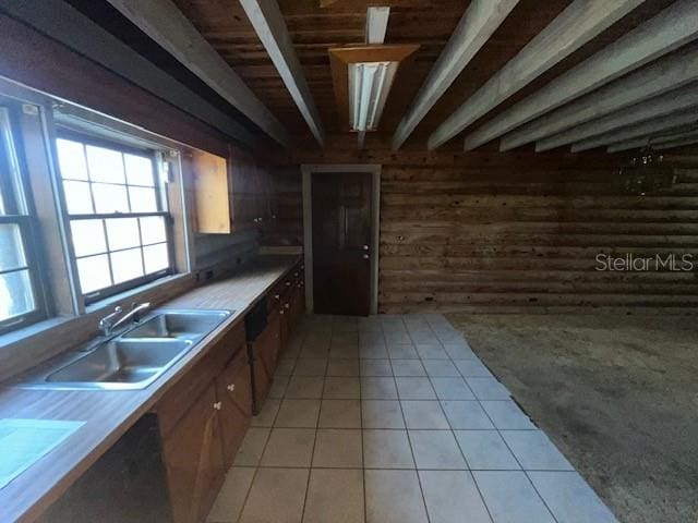 kitchen with light tile floors, wood walls, beamed ceiling, and sink