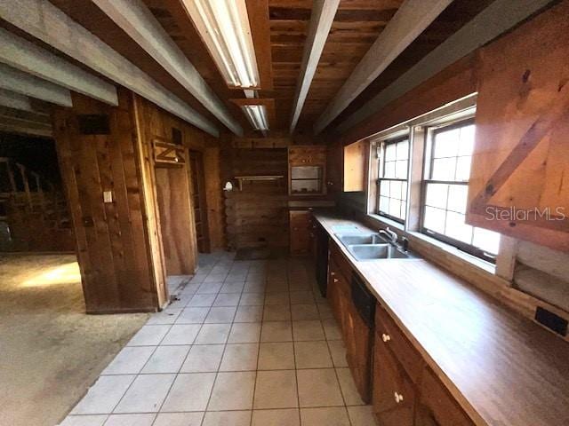 kitchen with beamed ceiling, sink, wood walls, and light tile floors