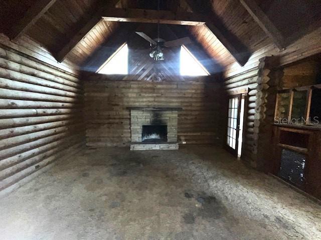 unfurnished living room featuring a stone fireplace, rustic walls, vaulted ceiling with beams, and wooden ceiling