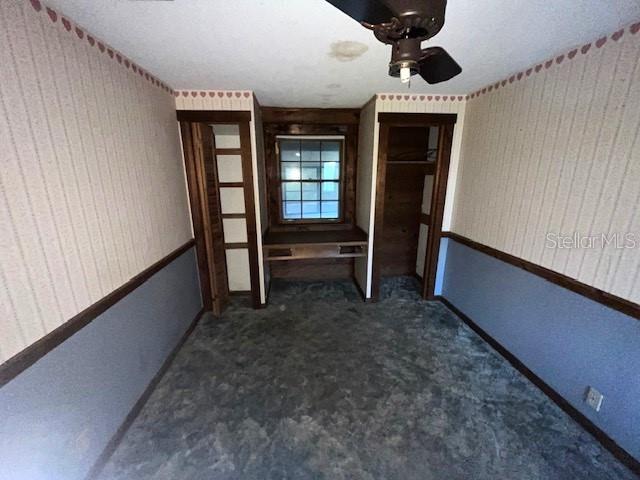 unfurnished bedroom with ceiling fan and dark colored carpet