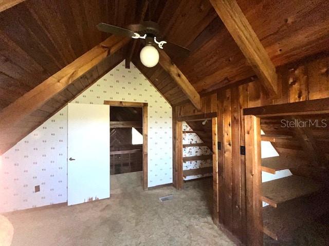 additional living space with wooden walls, dark colored carpet, lofted ceiling with beams, and wooden ceiling