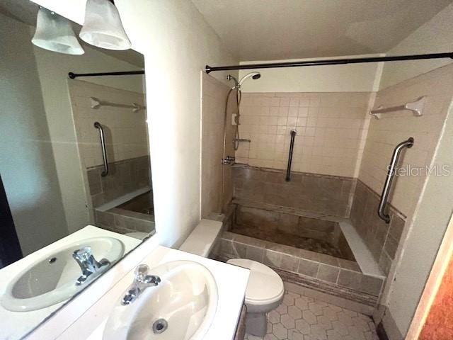 bathroom featuring tile flooring, sink, toilet, and a tile shower