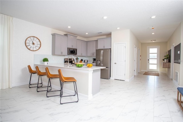 kitchen with kitchen peninsula, stainless steel appliances, backsplash, gray cabinetry, and a breakfast bar