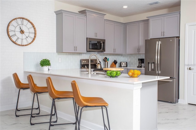 kitchen featuring light tile flooring, kitchen peninsula, backsplash, a kitchen breakfast bar, and appliances with stainless steel finishes