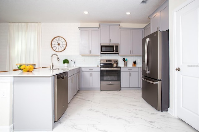 kitchen featuring kitchen peninsula, backsplash, gray cabinetry, appliances with stainless steel finishes, and sink