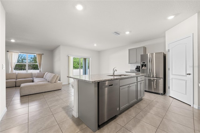 kitchen featuring gray cabinets, appliances with stainless steel finishes, light tile floors, sink, and an island with sink