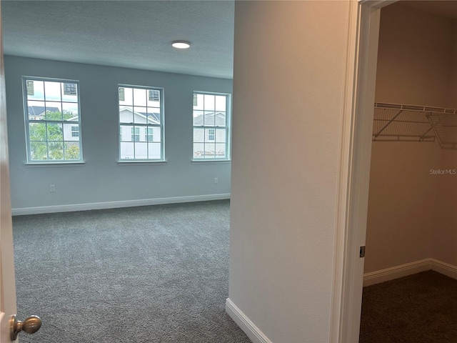 interior space with a spacious closet, a closet, a textured ceiling, and dark colored carpet