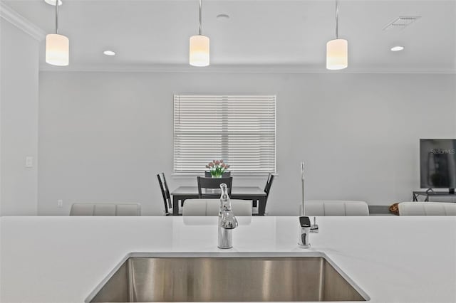 kitchen featuring hanging light fixtures, sink, light stone countertops, and crown molding