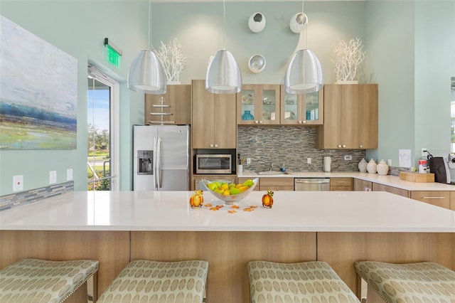 kitchen featuring a breakfast bar, light brown cabinetry, backsplash, decorative light fixtures, and stainless steel appliances