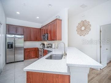 kitchen with appliances with stainless steel finishes, light hardwood / wood-style flooring, sink, and kitchen peninsula