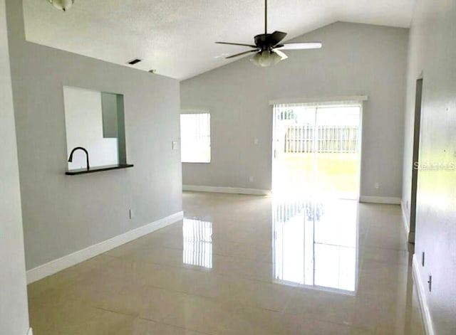 spare room with a wealth of natural light, tile flooring, ceiling fan, and vaulted ceiling