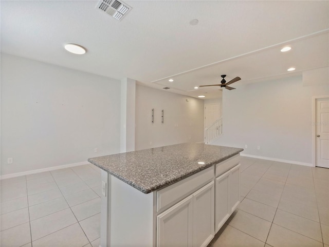 kitchen featuring dark stone counters, ceiling fan, a kitchen island, light tile floors, and white cabinetry