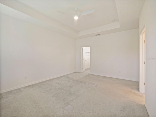 unfurnished room with ceiling fan, a tray ceiling, and light carpet