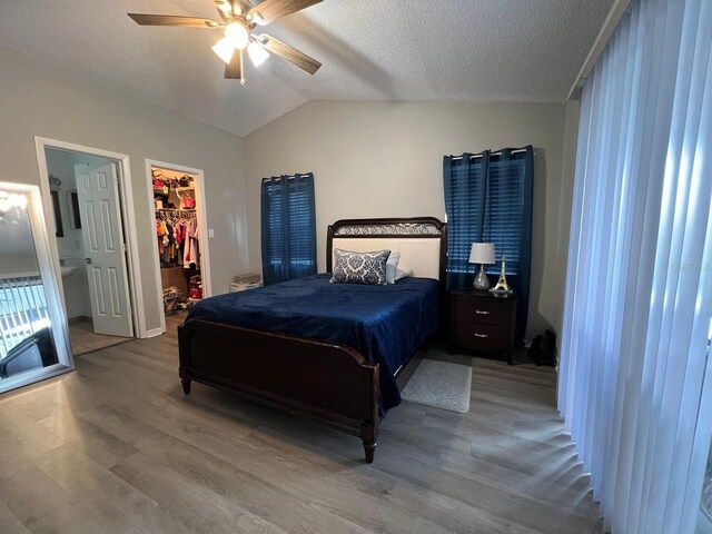 bedroom with ceiling fan, a spacious closet, light hardwood / wood-style flooring, vaulted ceiling, and a textured ceiling