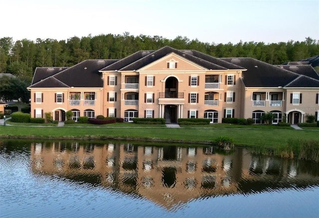 back of property featuring a yard, a water view, and a balcony