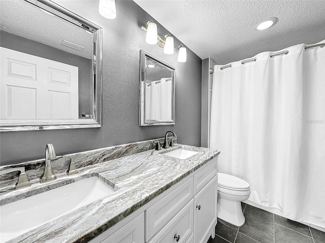 bathroom with tile floors, toilet, dual bowl vanity, and a textured ceiling