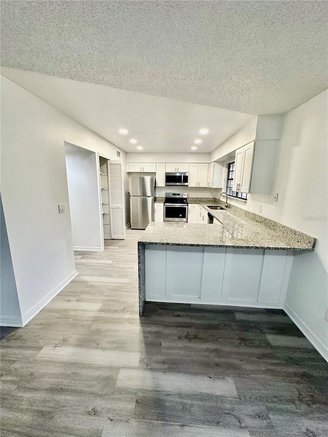 kitchen featuring light stone countertops, sink, stainless steel appliances, kitchen peninsula, and white cabinets