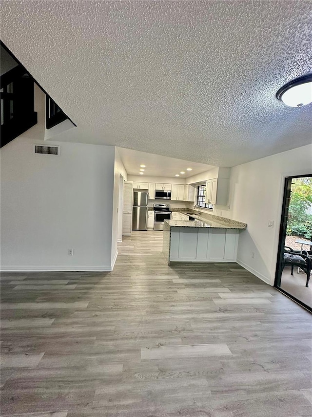 kitchen featuring light hardwood / wood-style flooring, kitchen peninsula, a textured ceiling, white cabinets, and appliances with stainless steel finishes