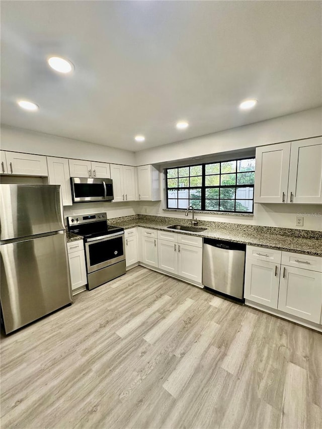 kitchen featuring white cabinets, sink, dark stone countertops, appliances with stainless steel finishes, and light hardwood / wood-style floors