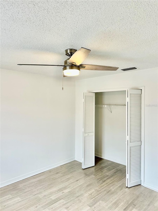 unfurnished bedroom with ceiling fan, a closet, a textured ceiling, and light wood-type flooring