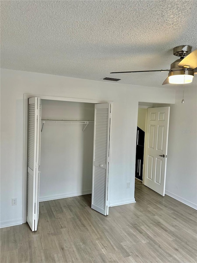 unfurnished bedroom featuring ceiling fan, a closet, a textured ceiling, and light wood-type flooring