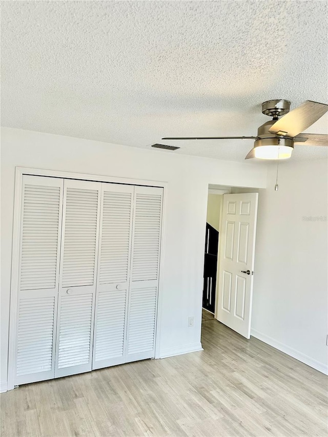 unfurnished bedroom with ceiling fan, light hardwood / wood-style floors, a textured ceiling, and a closet