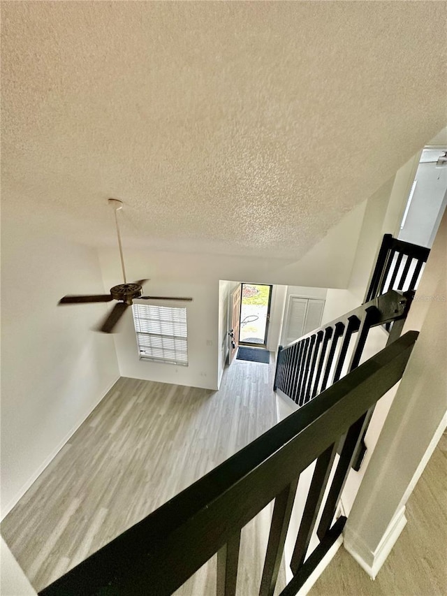 staircase with wood-type flooring, a textured ceiling, and ceiling fan