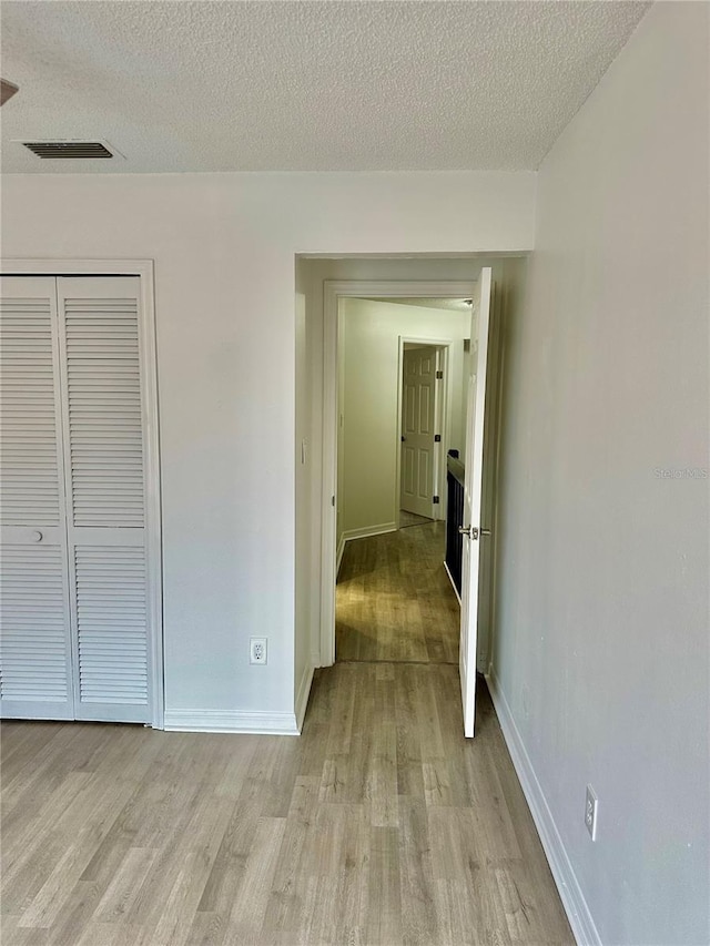 hallway featuring light wood-type flooring and a textured ceiling