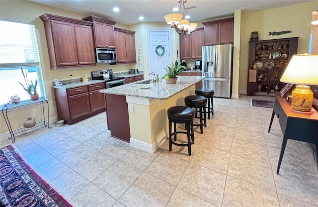 kitchen with hanging light fixtures, appliances with stainless steel finishes, a kitchen bar, sink, and an island with sink