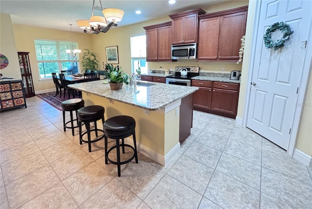 kitchen featuring pendant lighting, a kitchen island with sink, stainless steel appliances, light tile floors, and a notable chandelier