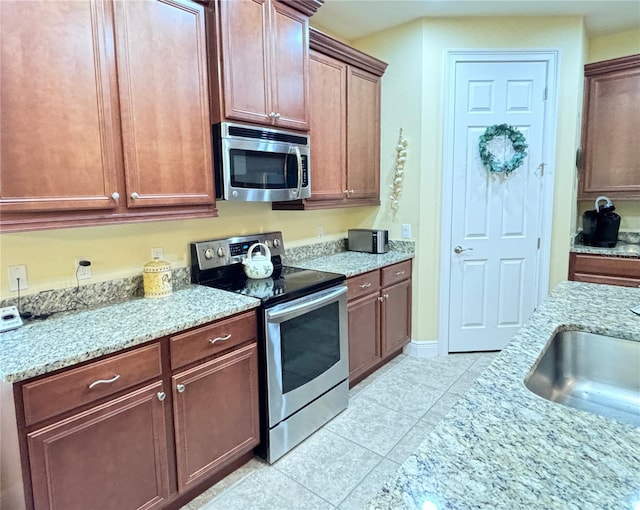 kitchen featuring sink, stainless steel appliances, light tile floors, and light stone countertops