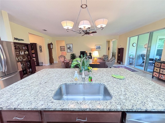 kitchen featuring light stone counters, sink, a notable chandelier, stainless steel fridge, and pendant lighting