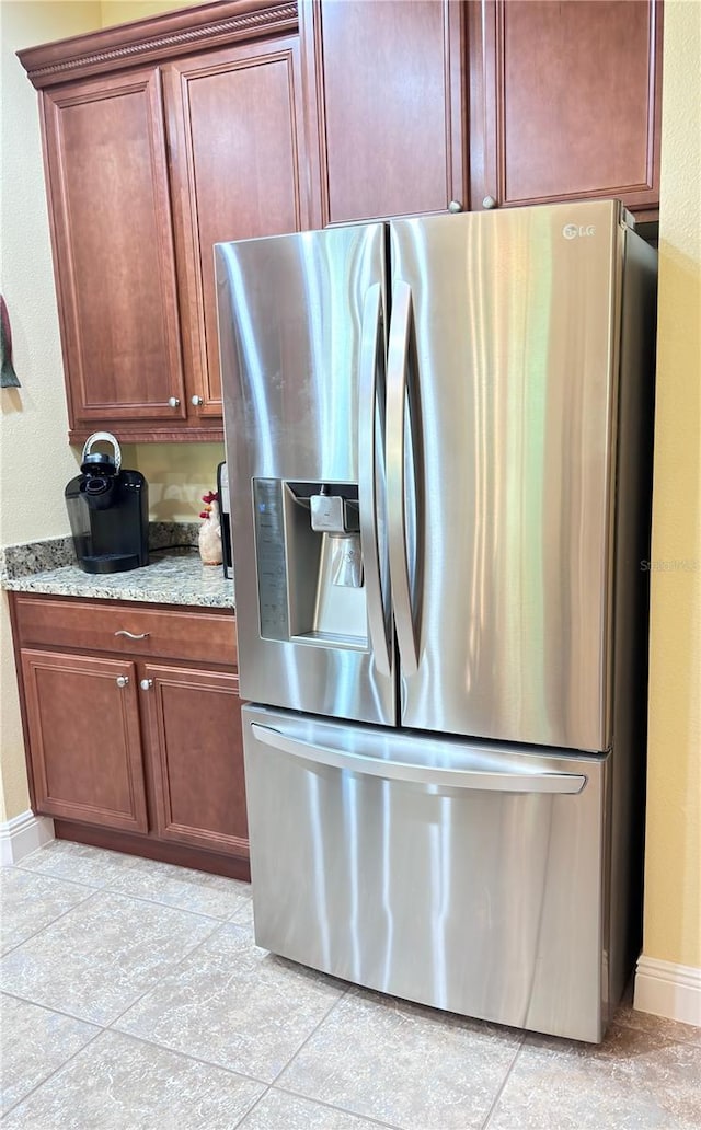 kitchen with light tile flooring, stainless steel refrigerator with ice dispenser, and light stone countertops