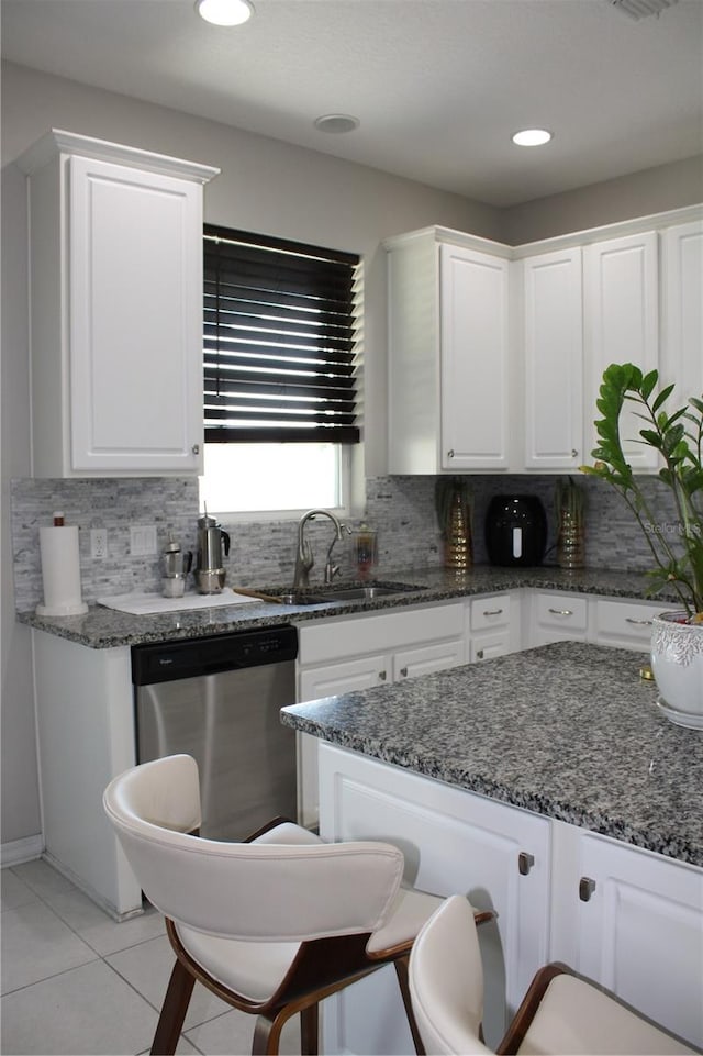 kitchen with tasteful backsplash, dark stone countertops, white cabinetry, and stainless steel dishwasher