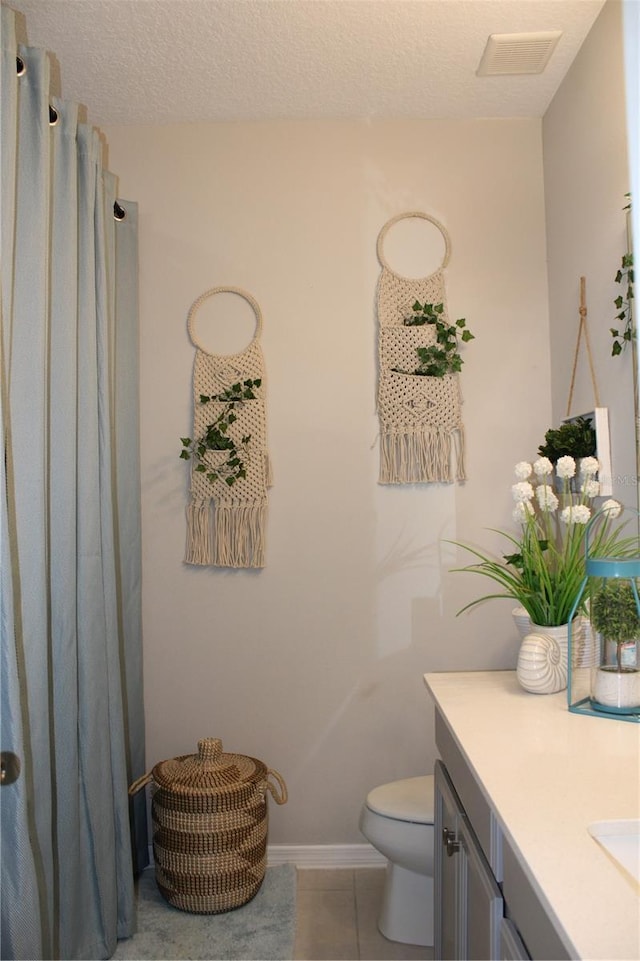 bathroom with tile floors, vanity, toilet, and a textured ceiling