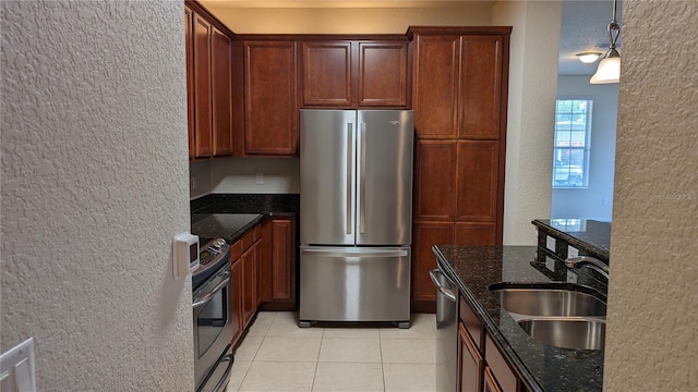 kitchen with stove, dark stone counters, stainless steel refrigerator, sink, and light tile floors