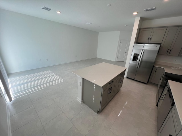 kitchen featuring stainless steel refrigerator with ice dispenser, a center island, light tile floors, and gray cabinetry