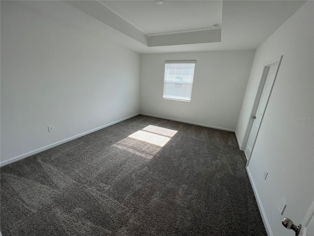 empty room featuring a tray ceiling and dark colored carpet