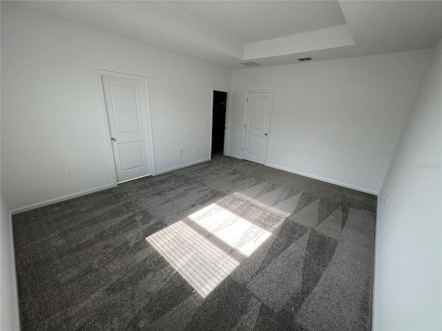 unfurnished bedroom with a raised ceiling and dark colored carpet