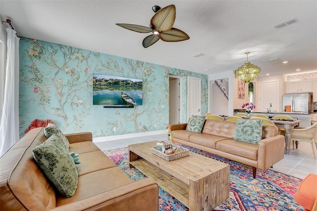 living room featuring ceiling fan with notable chandelier, light tile patterned flooring, sink, and a textured ceiling