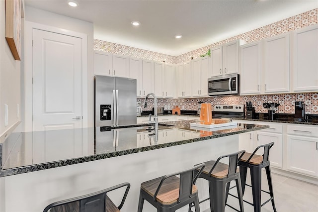 kitchen with dark stone countertops, a breakfast bar, white cabinets, and appliances with stainless steel finishes