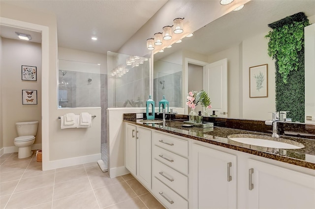 bathroom featuring tile patterned flooring, a tile shower, vanity, and toilet