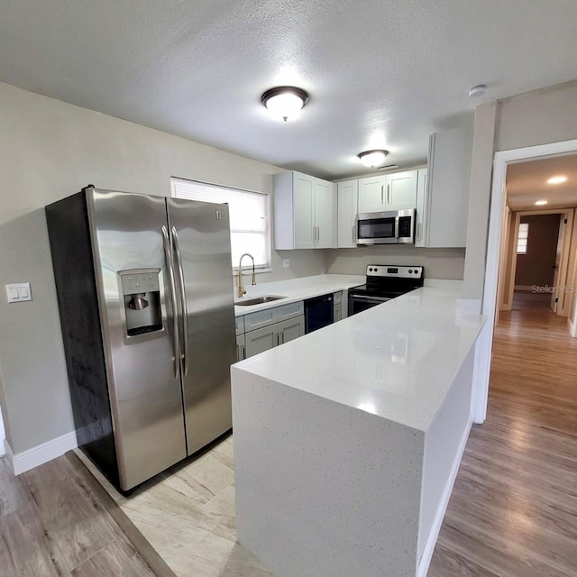 kitchen with light wood-type flooring, white cabinetry, stainless steel appliances, sink, and a textured ceiling