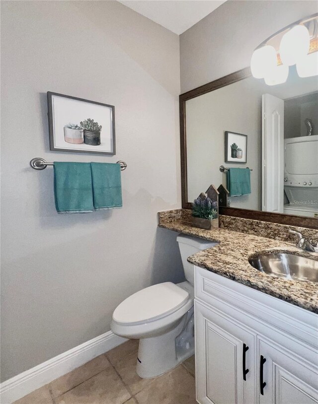 half bathroom with stacked washer and dryer, toilet, vanity, baseboards, and tile patterned floors