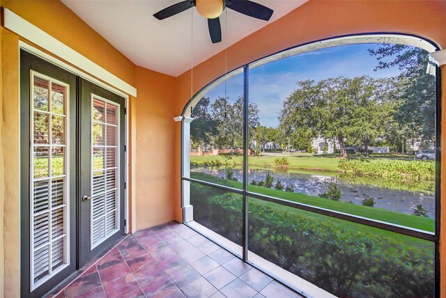 unfurnished sunroom featuring a water view, ceiling fan, and french doors