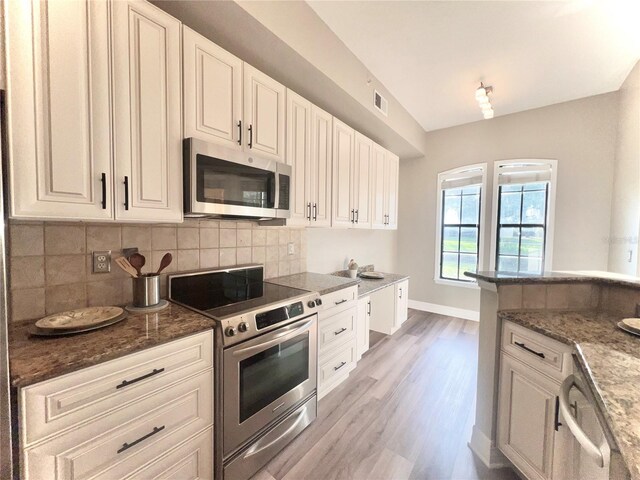 kitchen featuring dark stone countertops, stainless steel appliances, light wood-style floors, white cabinetry, and backsplash