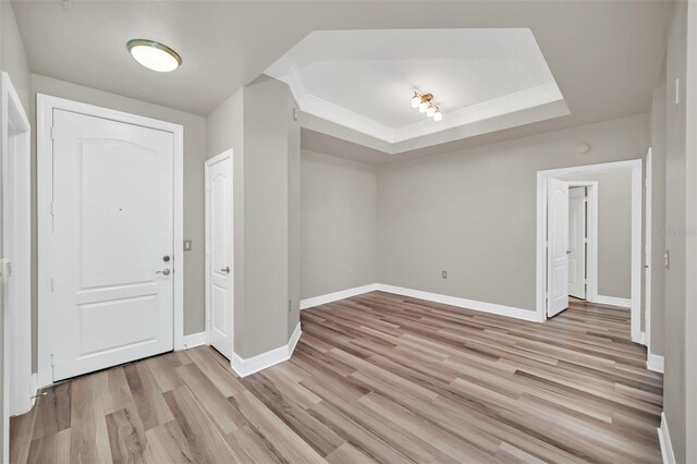 foyer featuring light wood finished floors, baseboards, a tray ceiling, and ornamental molding