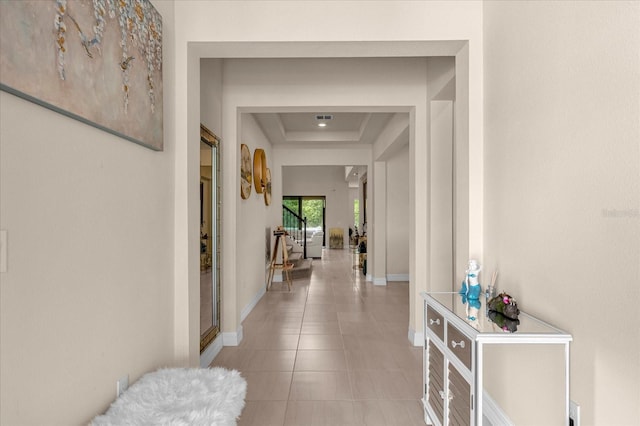 hallway featuring light tile patterned floors and a tray ceiling